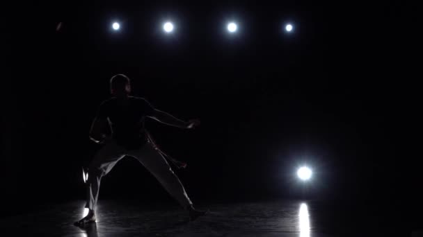 Hombre practicando capoeira contra proyectores en el estudio. Movimiento lento . — Vídeo de stock