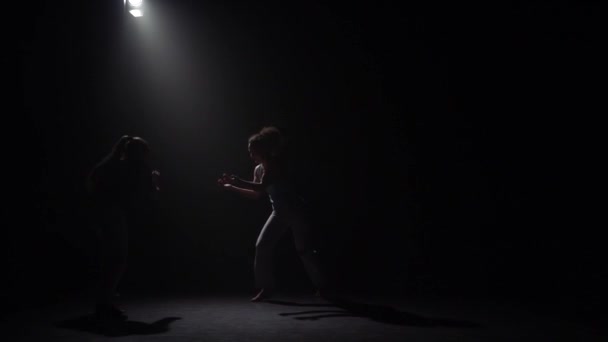 Dos mujeres practicando capoeira en la oscuridad bajo el foco de atención en el estudio. Movimiento lento . — Vídeo de stock