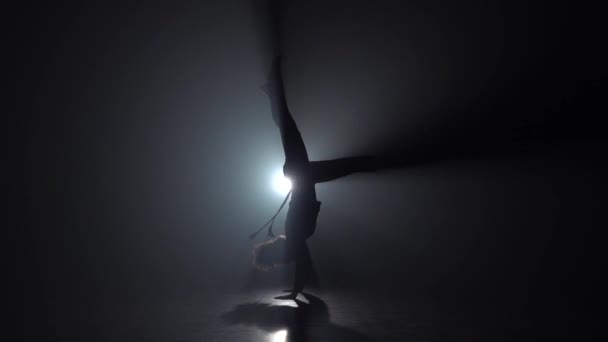 Капоэйра в исполнении женщины в темной студии против фары. Медленное движение — стоковое видео