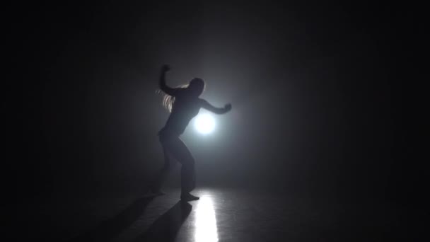 Dama hábil practicando capoeira en la oscuridad contra el proyector en el estudio. Movimiento lento . — Vídeos de Stock