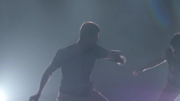 Acercamiento chicos practicando capoeira en la oscuridad contra proyector en el estudio, cámara lenta — Vídeos de Stock