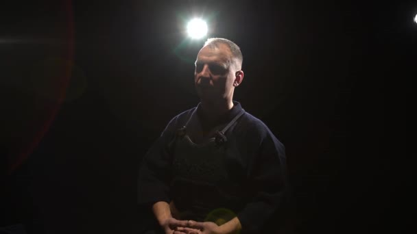 Kendo guru sitting on floor with closed eyes at background spotlights — Stock Video