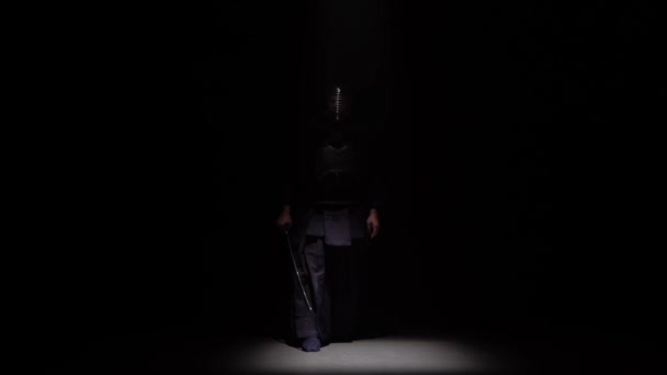 Zawodnik Kendo wykonujący sztukę walki z mieczem katana w ciemnym studiu pod reflektorem. — Wideo stockowe