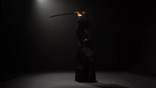 Zawodnik Kendo wykonujący sztukę walki z mieczem katana w ciemnym studiu pod reflektorem. — Wideo stockowe