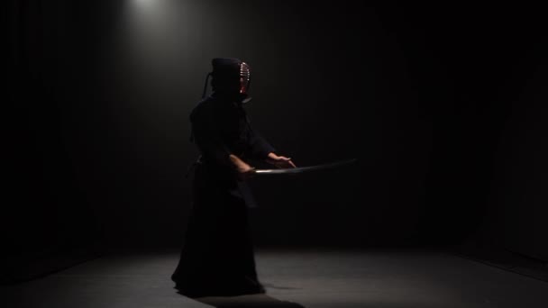 Kendo fighter performing martial art with Katana sword at dark studio under spotlight. — Stock Video