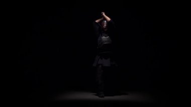 Kendo savaşçı spot altında karanlık stüdyoda Katana kılıç ile dövüş sanatı yapıyor. Yavaş çekim