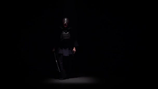 Боец Кендо, занимающийся боевым искусством с мечом Катаны в темной студии под прицелом. Медленное движение — стоковое видео