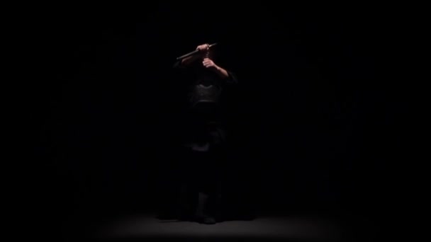 Caça Kendo executando arte marcial com Katana espada no estúdio escuro sob holofotes. Movimento lento — Vídeo de Stock
