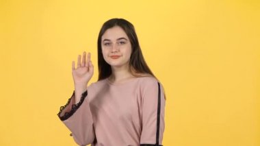 Genç kız elleriyle sarı arka planda el sallıyor. Yavaş çekim