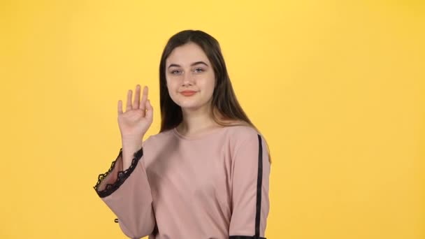 Chica joven saludando con las manos sobre fondo amarillo. Movimiento lento — Vídeos de Stock