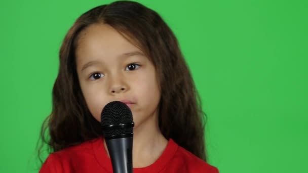 Primo piano bambino dai capelli scuri con microfono su sfondo verde. Rallentatore — Video Stock