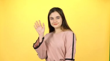 Genç kız sarı arka plan üzerinde elleri ile el sallayarak