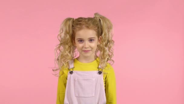 Смішна кучерява дівчинка сміється в студії на рожевому фоні — стокове відео