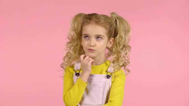 Chica joven rubia bonita es reflexivo en el estudio sobre fondo rosa — Vídeos de Stock
