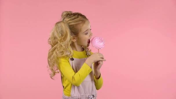 Красивая девушка пробует розовые конфеты на палочке — стоковое видео