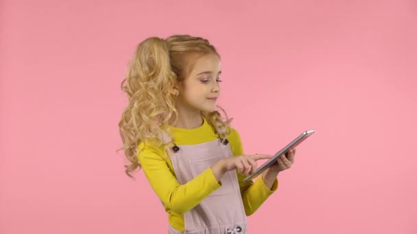Досить маленька дівчинка грає з планшетом і відправляє ударний поцілунок . — стокове відео