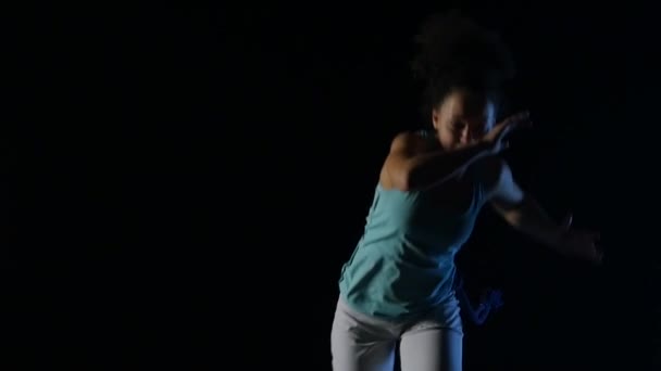 Primer plano rizado hembra practicando capoeira en la oscuridad en el estudio. Movimiento lento — Vídeo de stock