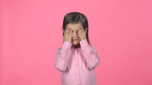 Kleine vrouw verbergt gezicht met handen op roze achtergrond. — Stockvideo