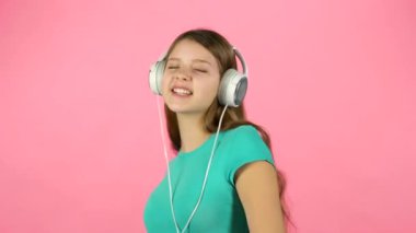 Kız müzik dinler ve pembe arka planda büyük beyaz kulaklıklar dansları