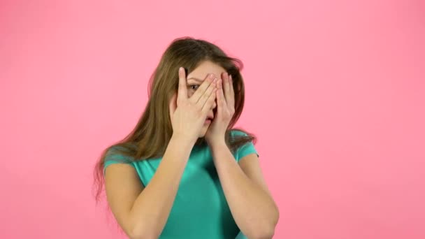 Pequeña hembra tiene miedo y esconde su cara en el estudio sobre fondo rosa . — Vídeos de Stock