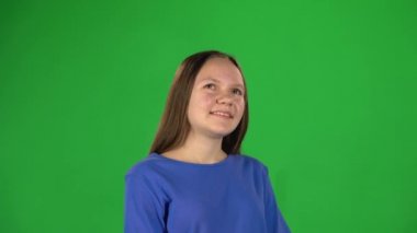 Yeşil arka planda kameraya bakarak gülümseyen kız.