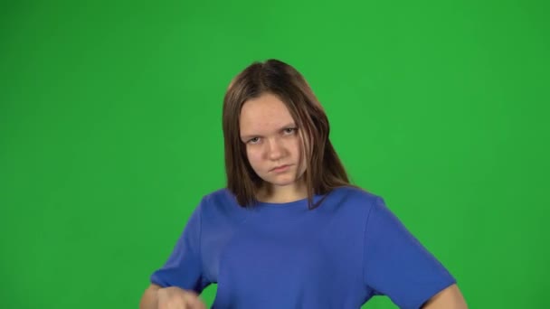 Flickan är arg och missnöjd stående med händerna på höfterna på grön bakgrund. — Stockvideo