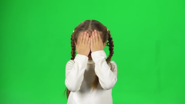 Маленька самка ховає обличчя руками на зеленому тлі . — стокове відео