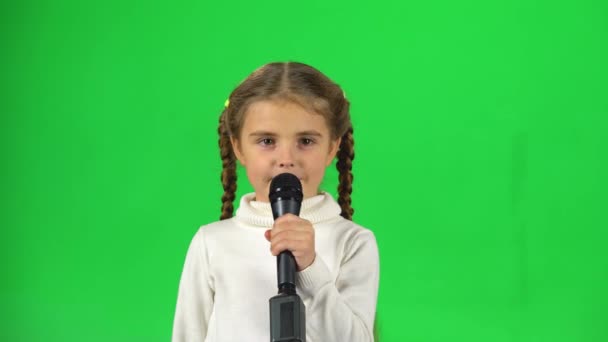 Маленькая девочка поет в микрофон на зеленом экране в студии — стоковое видео