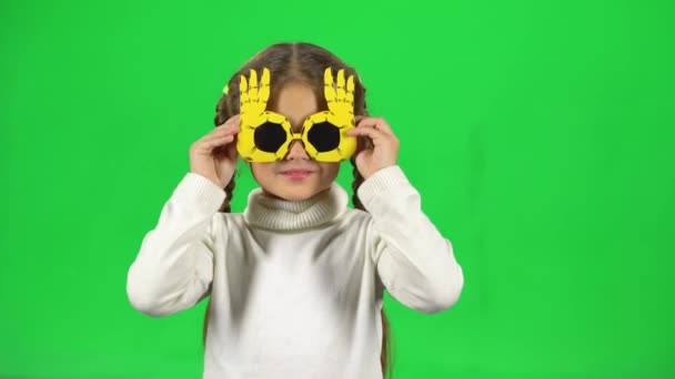 Ragazza carina in occhiali divertenti li toglie e mostra la lingua sullo schermo verde — Video Stock