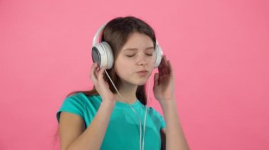 Kız müzik dinler ve pembe arka planda büyük beyaz kulaklıklar dansları. Yavaş çekim