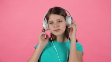 Küçük kadın müzik dinler ve pembe arka plan üzerinde büyük beyaz kulaklıklar dansları. Yavaş çekim
