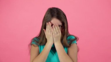 Kız korkuyor ve pembe arka plan üzerinde stüdyoda yüzünü gizleme. Yavaş çekim