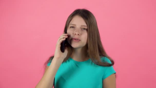 Adolescente mujer hablando usando el teléfono celular en el estudio contra el fondo rosa. Movimiento lento — Vídeos de Stock