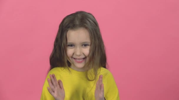 Una niña embrujada con sonrisa aplaude sobre un fondo rosado. Movimiento lento — Vídeo de stock
