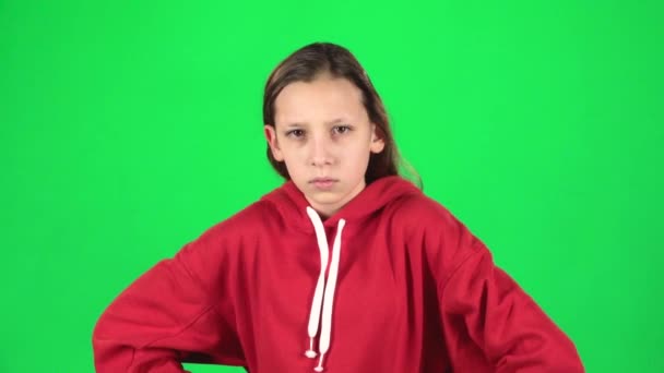 Schattig meisje is boos en ontevreden staan met handen op haar heupen op groene achtergrond. Slow Motion — Stockvideo