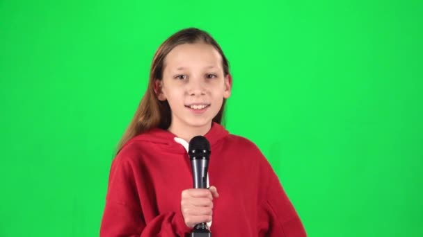 Κορίτσι τραγουδώντας σε ένα μικρόφωνο σε πράσινο φόντο στο στούντιο. Αργή κίνηση — Αρχείο Βίντεο