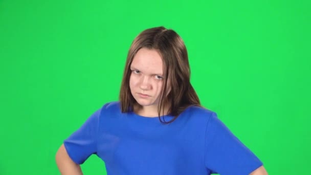 Girl is angry and unsatisfied standing with hands at her hips on green background. Slow motion — Stock Video