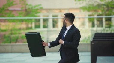 Takım elbiseli neşeli ve mutlu bir işadamı, sokak meydanında aktif olarak dans ediyor. Olay yeri, bir iş merkezinin yanındaki beton parkta çekildi. Güneşli bir gün.