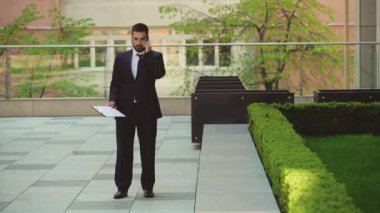 Çok öfkeli işadamı bir tablet ile sokakta yürür ve cep telefonu konuşuyor.