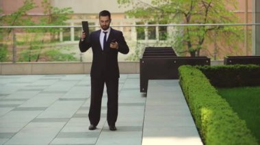 Çok öfkeli işadamı bir tablet ile sokakta yürür ve cep telefonu konuşuyor.