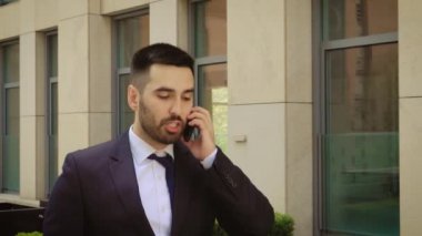 Genç işadamı ofis binası nın yakınında açık havada cep telefonuyla konuşurken rahatsız oldu. Adam kızgın ve üzgün.