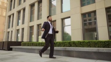 Mutlu işadamı ofis merkezi nin yakınındaki sokakta dans ediyor ve başarılarını kutlayan takım elbise giyiyor. Steadicam atış.