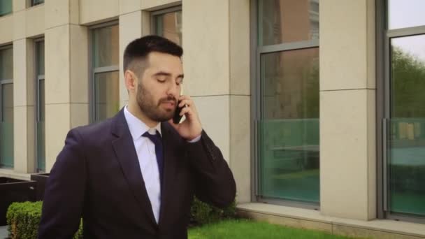 Emocional joven sonriente hablando en el teléfono inteligente al aire libre. Emocionado hombre de negocios feliz de escuchar buenas noticias mientras habla por teléfono celular — Vídeos de Stock