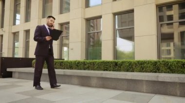 Etkileyici işadamı bir tablet ile sokakta yürüyor ve cep telefonu konuşuyor.