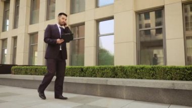 Çok öfkeli işadamı bir tablet ile sokakta yürür ve cep telefonu konuşuyor.