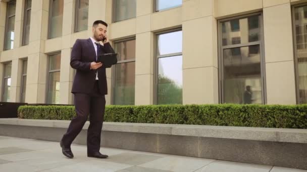 Hombre de negocios muy enojado camina por la calle con una tableta y hablando por teléfono móvil . — Vídeos de Stock