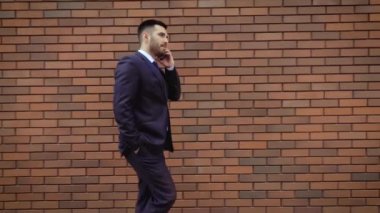 Modern bir tuğla duvarın arka planda yürürken gömlek konuşan akıllı telefon giymiş işadamı. Yakın çekim