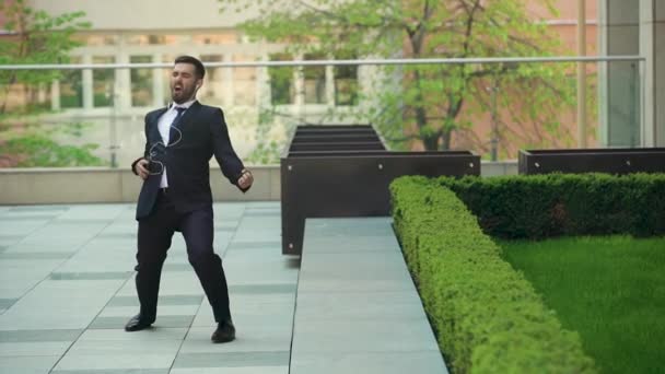 스마트 폰에서 헤드폰으로 음악을 듣고, 사무실 밖을 걷고, 리듬에 재미있는 춤을 추는 행복한 사업가. — 비디오