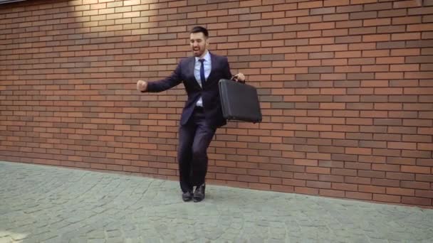 Привлекательный мужчина с бородой и портфелем, танцующий на городской улице. На фоне современной кирпичной стены . — стоковое видео