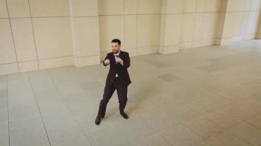 Siyah takım elbiseli ve kırmızı kravatlı işadamının şehirde dans eden ve zıplayan bir şekilde çekilmiş fotoğrafı. Yaptığı anlaşmadan çok memnun..